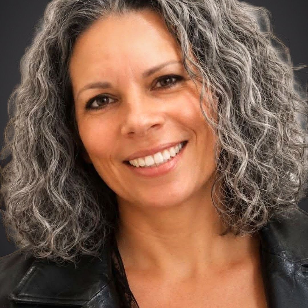 Portrait de Caroline Pauzé, souriante, cheveux gris bouclés, veste de cuir noire